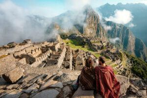 Couple dressed in ponchos watching the ruins of Machu Picchu, Peru