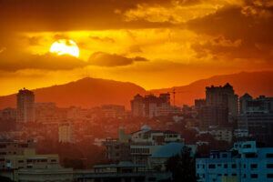 Sunset, Santo Domingo, Domenican Republic, large sun, cloudy sky, orange mood, mountains in background, romantic urban scape.