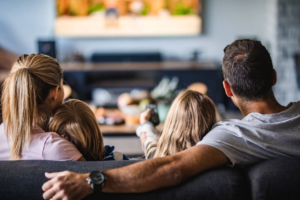 Back view of a relaxed family watching TV on sofa in the living room