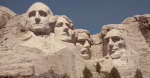 The faces of George Washington, Thomas Jefferson, Theodore Roosevelt, and Abraham Lincoln carved into Mount Rushmore in South Dakota against a blue sky.