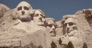 The faces of George Washington, Thomas Jefferson, Theodore Roosevelt, and Abraham Lincoln carved into Mount Rushmore in South Dakota against a blue sky.